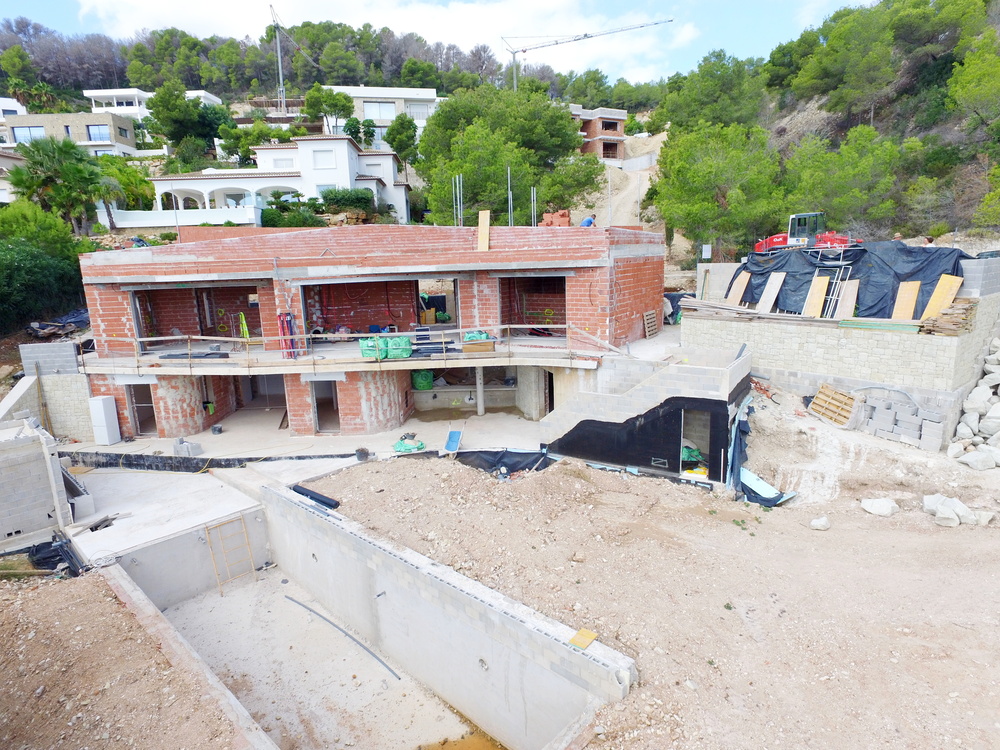 Bauphase einer zweistöckigen Villa mit Rohbau aus roten Ziegeln und Betonpool-Becken auf einem terrassierten Hanggrundstück inmitten von Pinien.