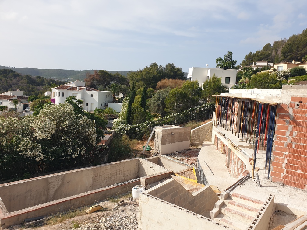 Baustelle einer Villa mit Betonfundamenten, Ziegelwänden mit Metallstützen und einem Pool-Aushub mit Blick auf ein mediterranes Tal.