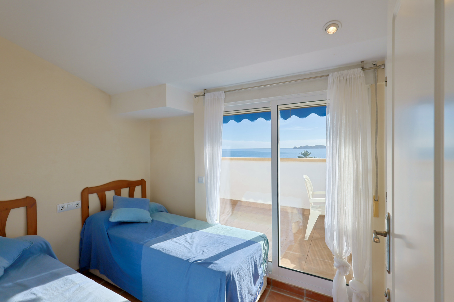 Helles Schlafzimmer mit zwei Einzelbetten und direktem Zugang zu einem privaten Balkon mit Panoramablick auf das Meer und die Küste. Terrakottafliesenboden und viel Tageslicht.
