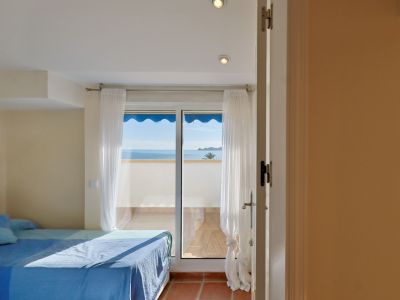 Helles Schlafzimmer mit blau bezogenem Bett und direktem Zugang zu einer Terrasse mit Panoramablick auf das Mittelmeer. Terrakottafliesen und weiße Vorhänge.