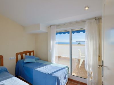 Helles Schlafzimmer mit zwei Einzelbetten und direktem Zugang zu einem privaten Balkon mit Panoramablick auf das Meer und die Küste. Terrakottafliesenboden und viel Tageslicht.