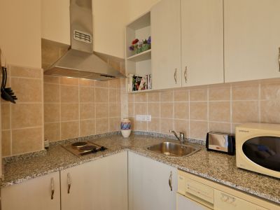 Kompakte Küche mit Granit-Effekt-Arbeitsplatten, beigem Fliesenspiegel und wesentlichen Geräten, darunter Kochfeld und Edelstahlspüle.