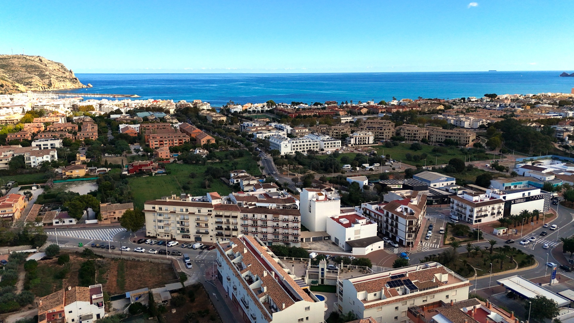Erhöhter Panoramablick auf die Stadtlandschaft von Jávea mit mediterraner Architektur, dem Hafenbereich und dem blauen Meer unter klarem Himmel.