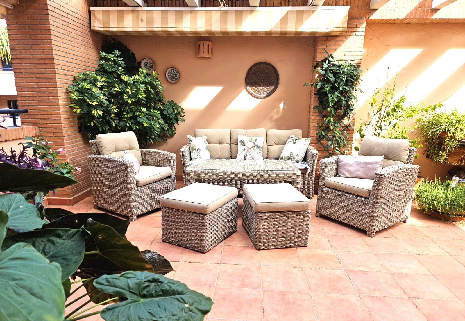 Private Terrasse mit Terrakottaboden, Lounge-Möbeln aus Polyrattan und ausziehbarer Markise, umrahmt von mediterraner Bepflanzung und Sichtmauerwerk.