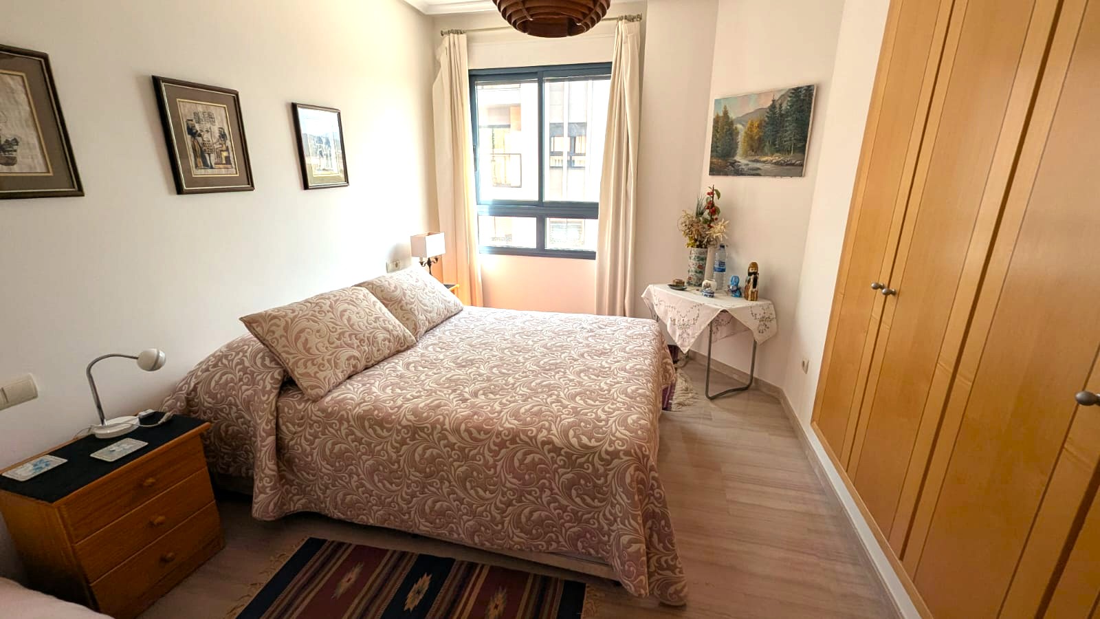 Schlafzimmer mit Einbauschränken aus Holz, hellem Laminatboden und Fenster mit natürlichem Licht. Funktionale Möbel und klassisches Dekor in warmen Farbtönen.