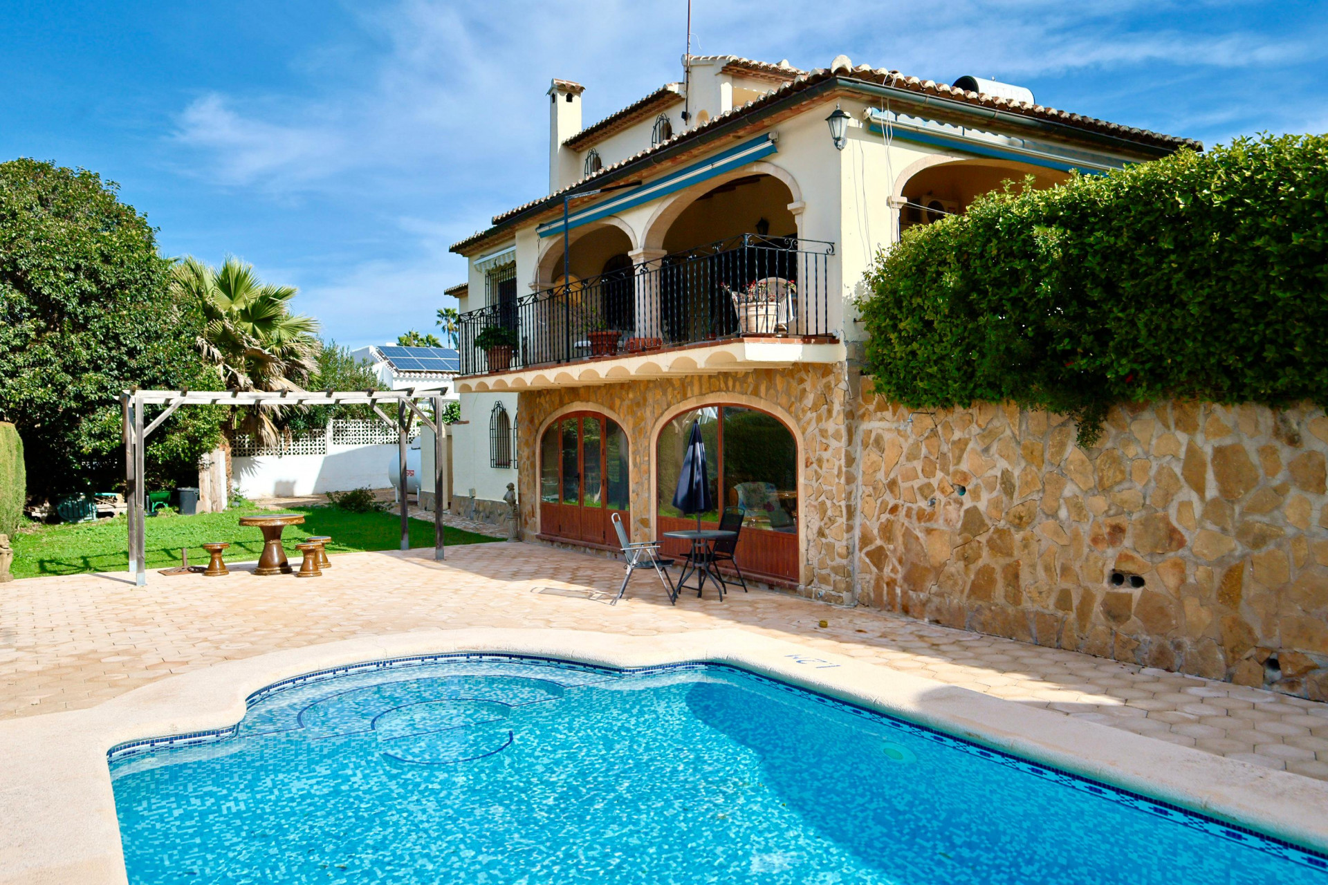 Außenansicht mit privatem Pool, Natursteinfassade, Rundbogenfenstern und großer überdachter Terrasse mit traditionellen Bögen und Schmiedeeisengeländer.