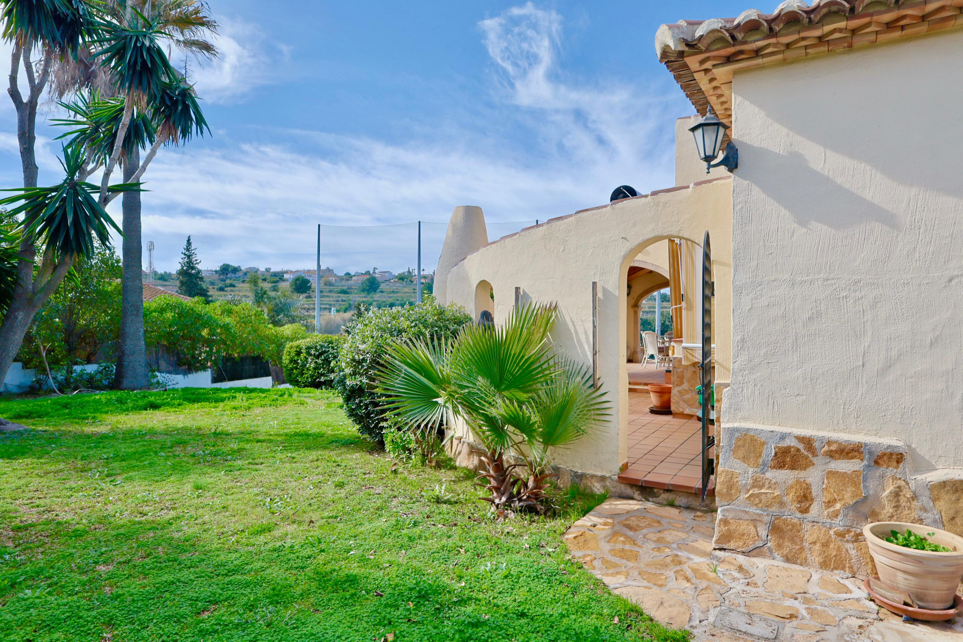 Außenfassade der Villa mit Natursteinsockel, mediterranem Garten und Rundbogeneingang zur Terracotta-Terrasse mit Blick auf die Golfplatzumgebung.