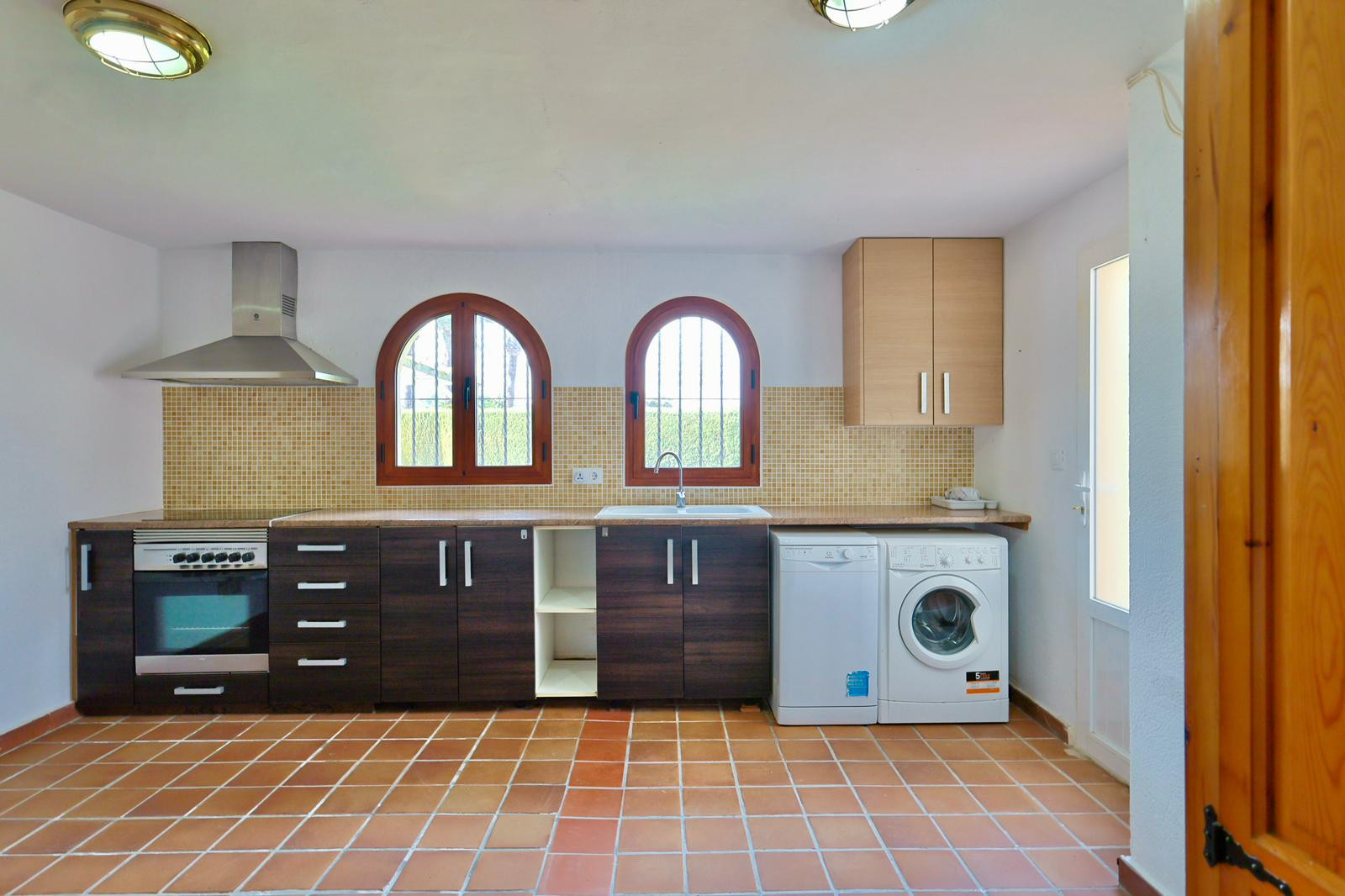 Praktische Küche mit Waschbereich, dunklen Schränken, Terrakottaboden und Rundbogenfenstern. Ausgestattet mit modernen Geräten und Mosaik-Fliesenspiegel.
