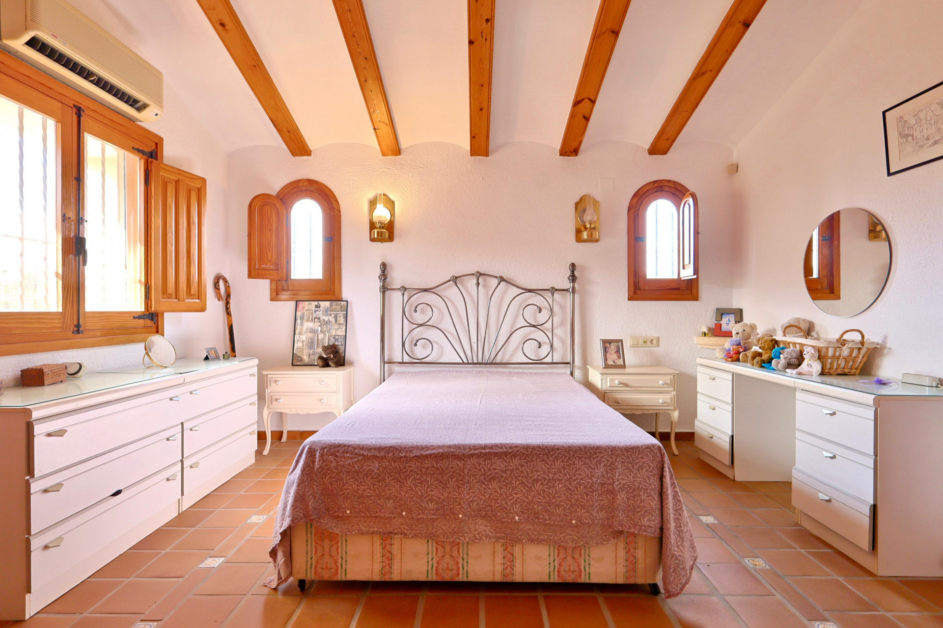 Schlafzimmer mit sichtbaren Holzbalken, Terrakottaboden und Rundbogenfenstern mit Holzläden. Mit einem Schmiedeeisenbett und einer Split-Klimaanlage ausgestattet.