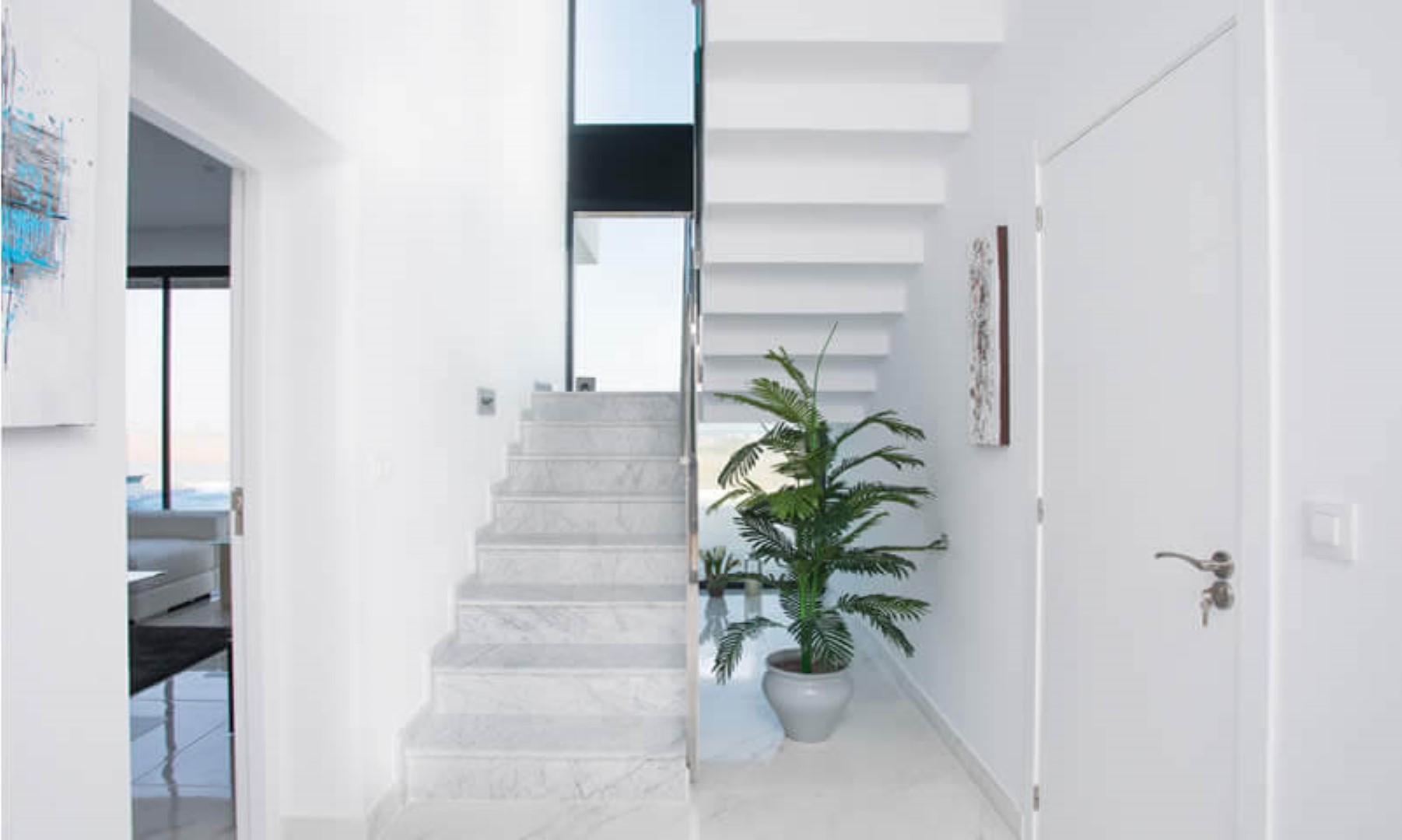 Minimalistischer Eingangsbereich mit Marmortreppe und weißen freitragenden Stufen, beleuchtet durch ein hohes vertikales Fenster für natürliches Licht.