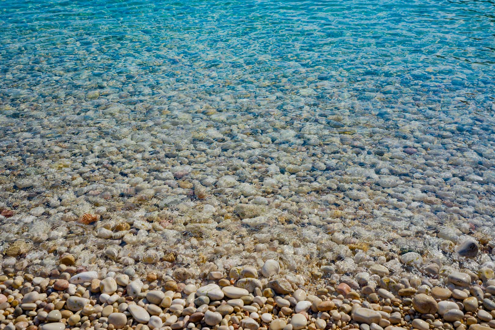 Detailansicht des kristallklaren, türkisfarbenen Wassers und der glatten weißen Kieselsteine am Strand von Granadella in der direkten Umgebung der Villa.