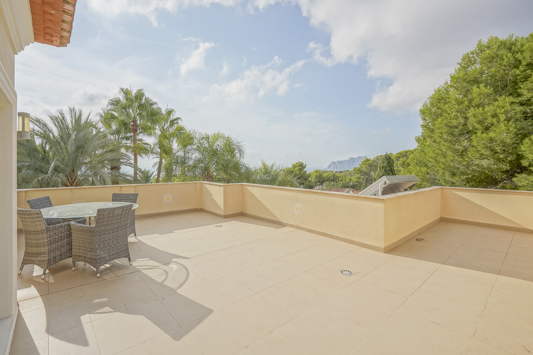 Großzügige Obergeschoss-Terrasse mit Fliesenboden und Gartenmöbeln, die einen weiten Blick auf den Peñón de Ifach und mediterrane Palmen bietet.
