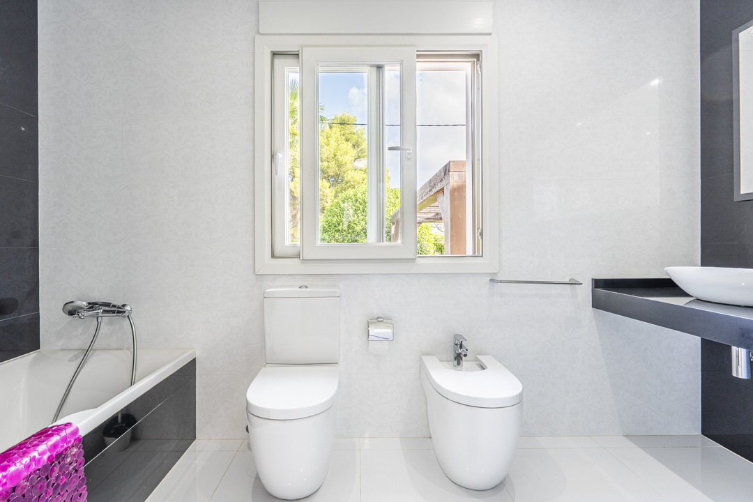 Modernes Badezimmer mit WC, Bidet und Badewanne. Es verfügt über einen schwarzen Waschtisch mit Aufsatzbecken, weiße Strukturfliesen und ein Fenster mit Blick ins Grüne.