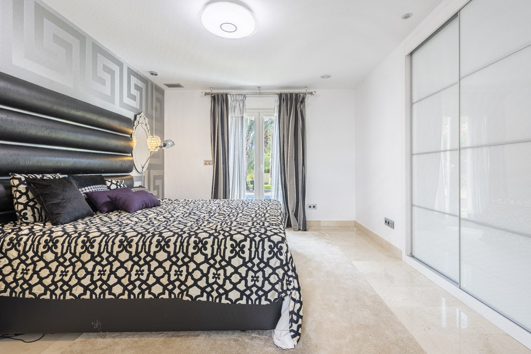 Schlafzimmer mit großem Einbauschrank mit weißen Schiebetüren, poliertem Marmorboden und direktem Zugang zum Garten durch Glastüren.