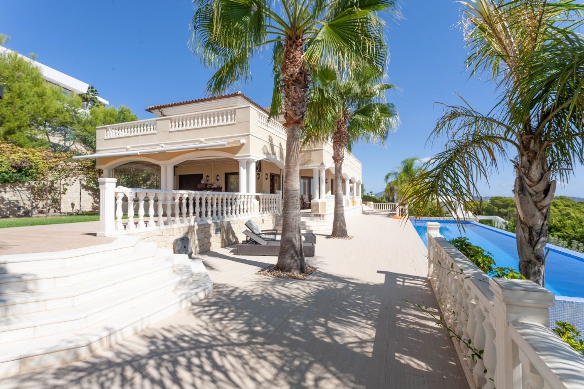 Außenbereich mit klassischer Balustrade, Palmen und einem Infinity-Pool neben der mediterranen Villa mit Rundbogen-Terrassen und Balkonen.
