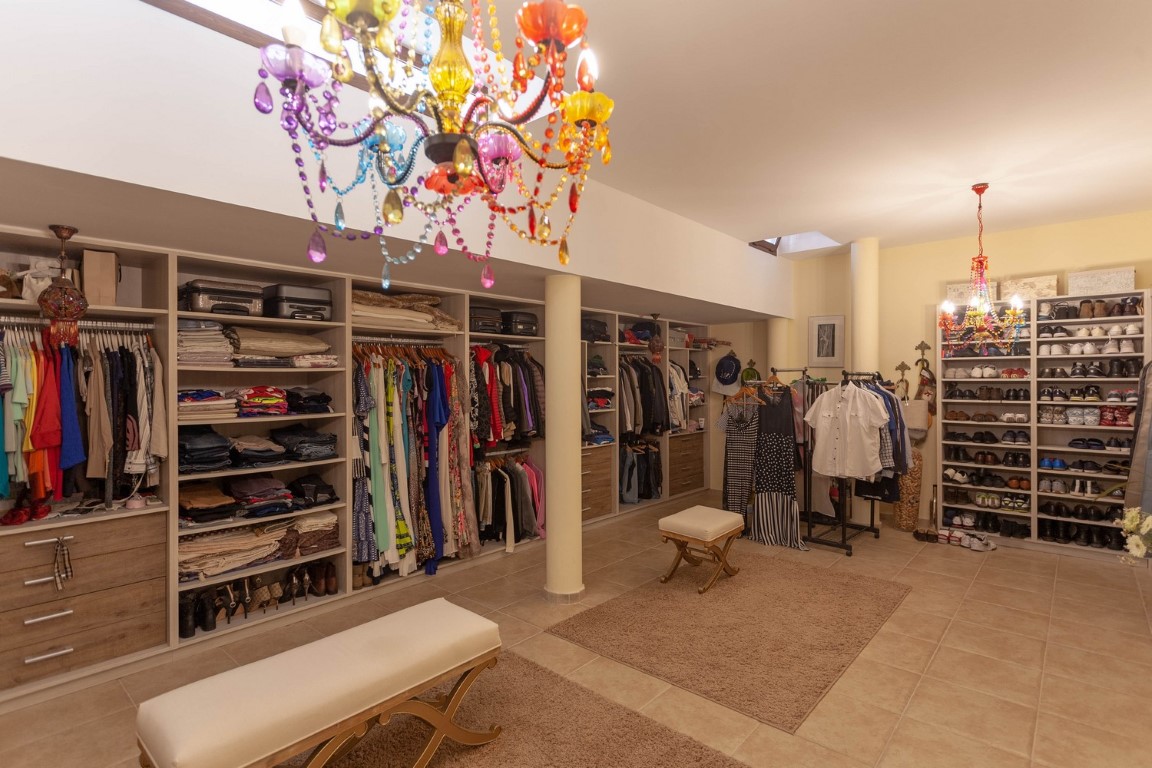 Begehbarer Kleiderschrank mit offenen Regalen, Holzschubladen und bunten Kristallleuchtern. Ausgestattet mit Polsterbänken, Oberlichtern und einem separaten Schuhregal.