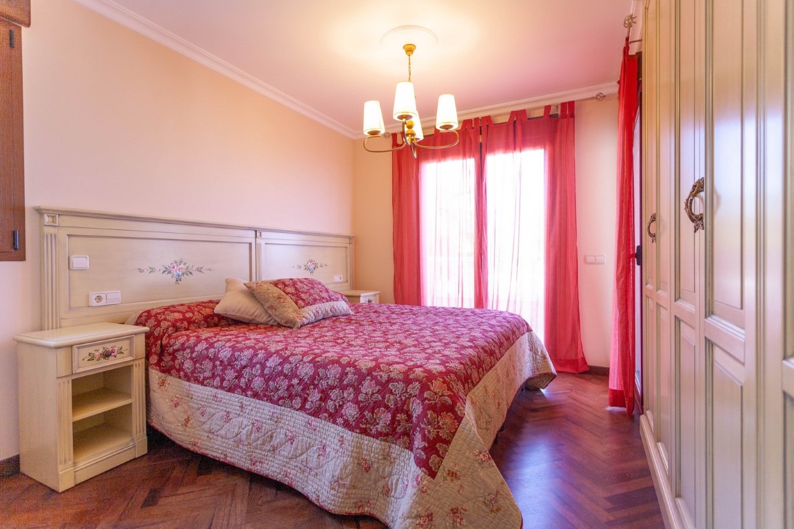 Schlafzimmer mit Fischgrätparkett, cremefarbenen Einbauschränken und Balkonzugang. Klassische Möbel mit floralen Motiven und rote Vorhänge ergänzen den Raum.
