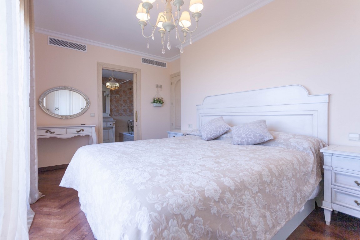 Schlafzimmer mit weißem Holzkopfteil, Parkettboden und Zugang zum En-Suite-Badezimmer mit Badewanne und klassischem Frisiertisch.