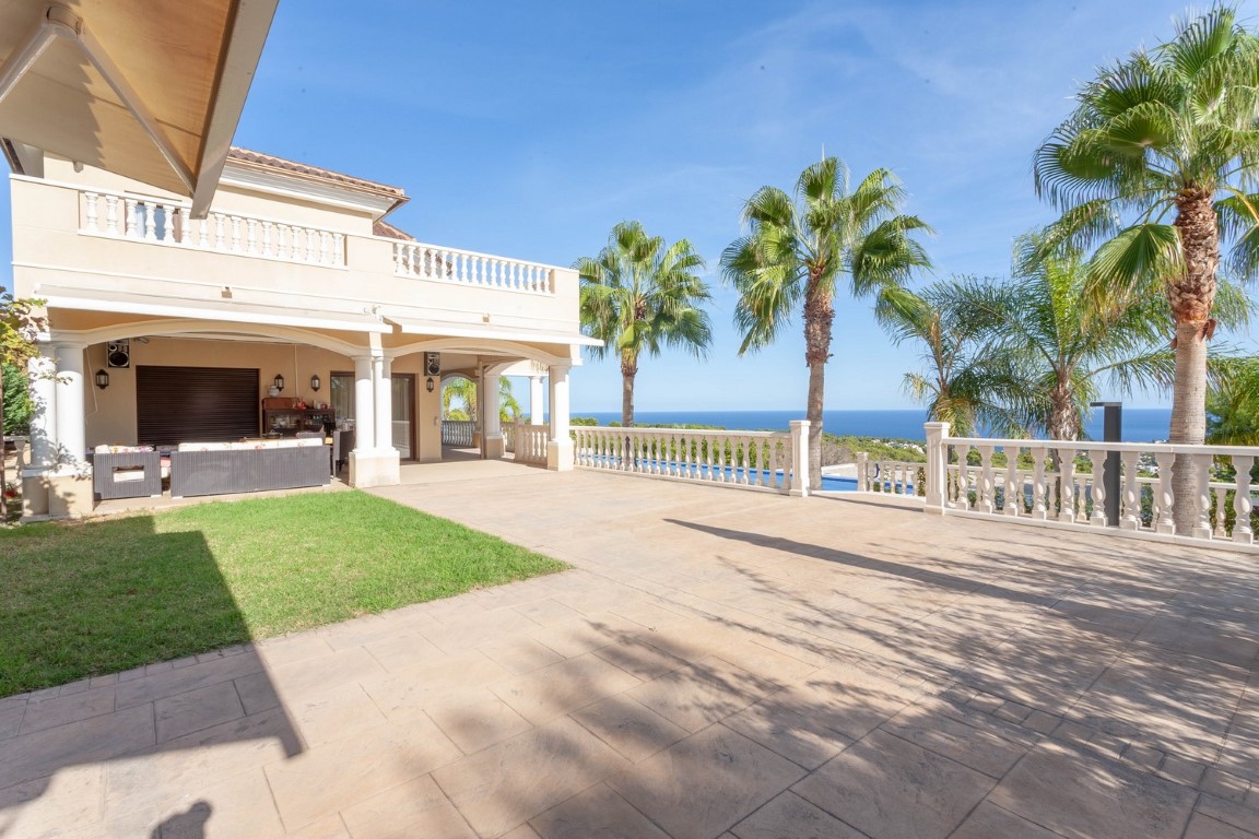 Weitläufige Steinterrasse mit klassischen weißen Balustraden und Panoramablick auf das Meer. Überdachte Veranda mit Sitzgelegenheiten und Palmen.