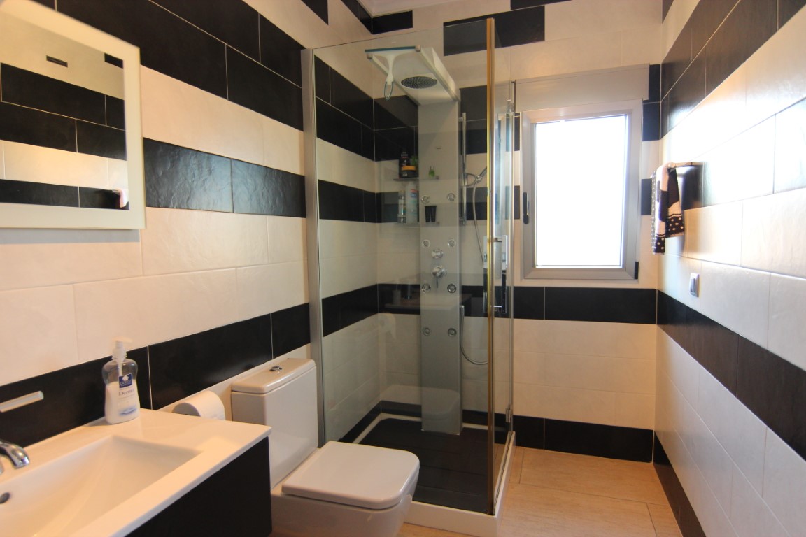 Badezimmer mit markanten schwarz-weiß gestreiften Fliesen, Glaskabine mit Hydromassage-Funktion und Außenfenster für Tageslicht.