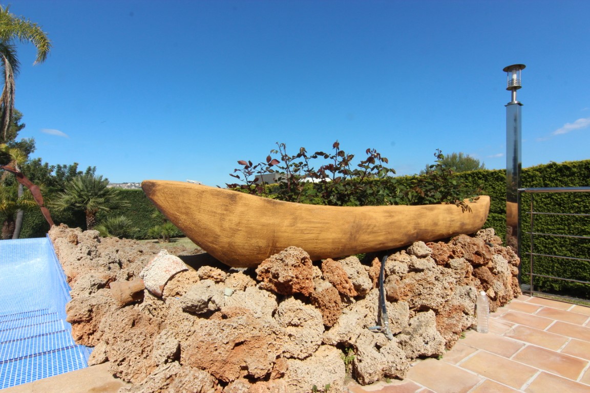Dekoratives Pflanzgefäß in Bootsform auf einer Natursteinmauer am Pool, umgeben von Terrakotta-Fliesen und mediterraner Bepflanzung.