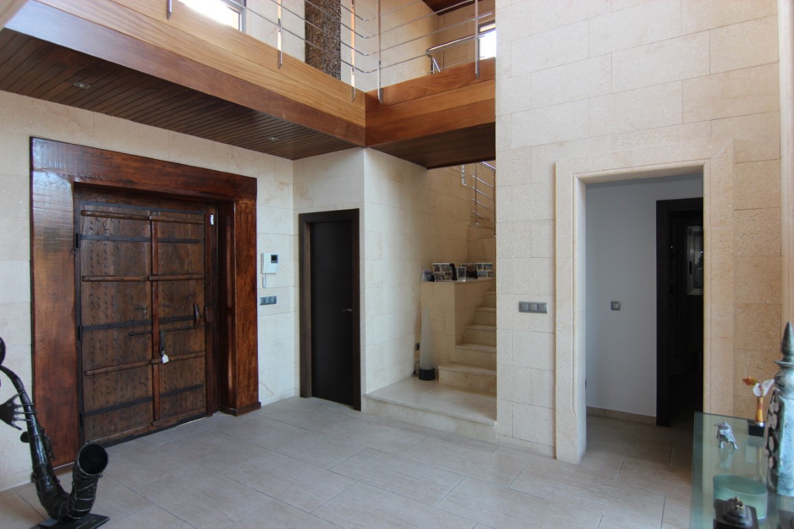 Doppelt hoher Eingangsbereich mit Natursteinwänden, einer großen rustikalen Holztür und einer oberen Galerie mit Holzdeckenpaneelen.