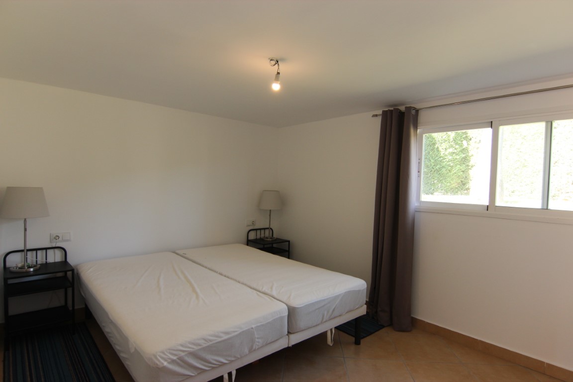 Doppelzimmer mit Fliesenboden, Schiebefenster mit Blick ins Grüne und minimalistischen Nachttischen aus schwarzem Metall.