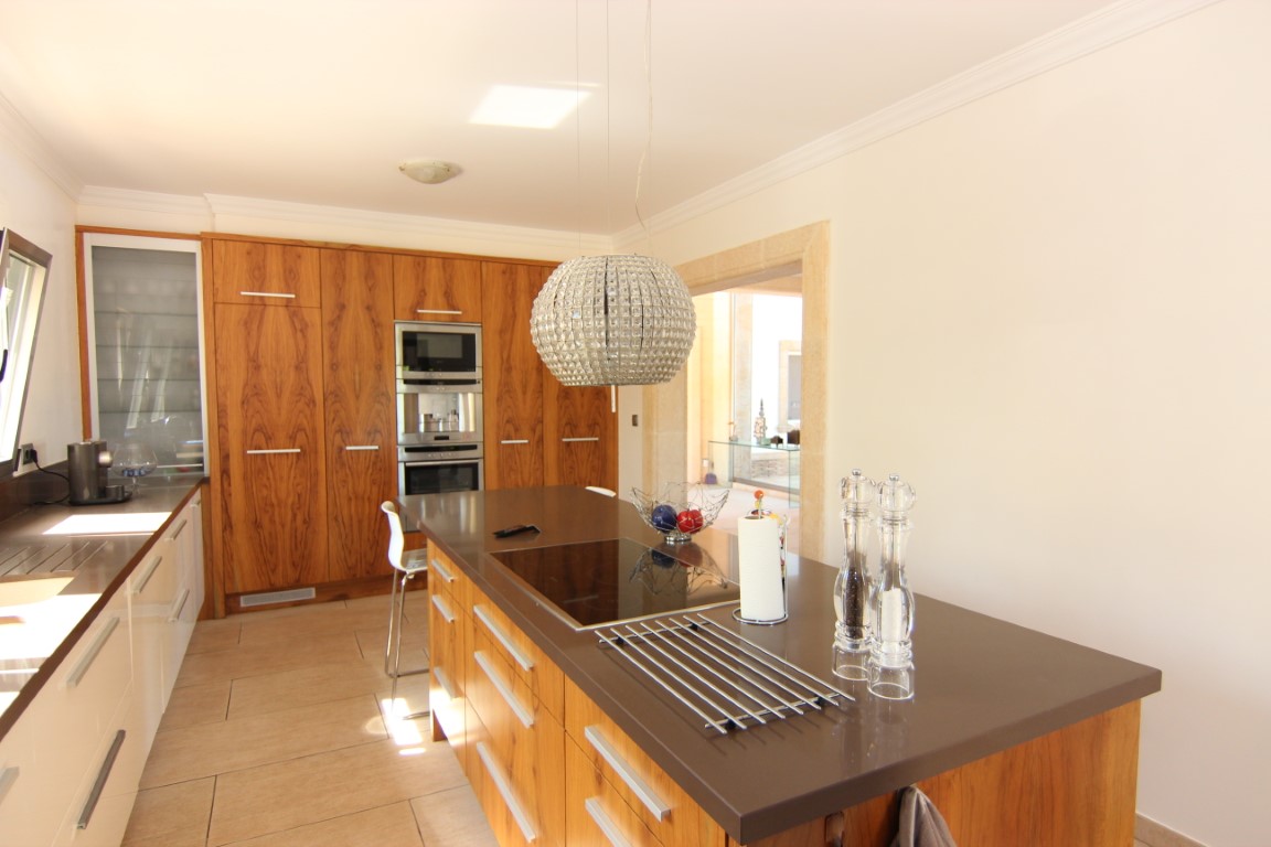 Moderne Küche mit zentraler Kochinsel, brauner Arbeitsplatte und Schränken aus Echtholz. Ausgestattet mit Einbaugeräten und einer eleganten kugelförmigen Pendelleuchte.