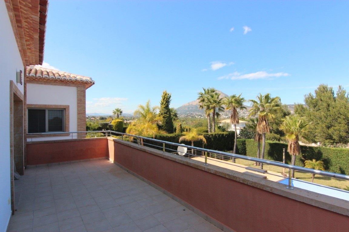 Obergeschoss-Terrasse mit Edelstahlgeländer und Steinabdeckung, mit weitem Blick über den Garten und Pool bis hin zum Berg Montgó.