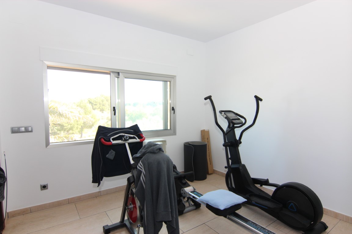 Privater Fitnessraum mit verschiedenen Trainingsgeräten, hellen Bodenfliesen und einem großen Fenster, das für viel Tageslicht sorgt.