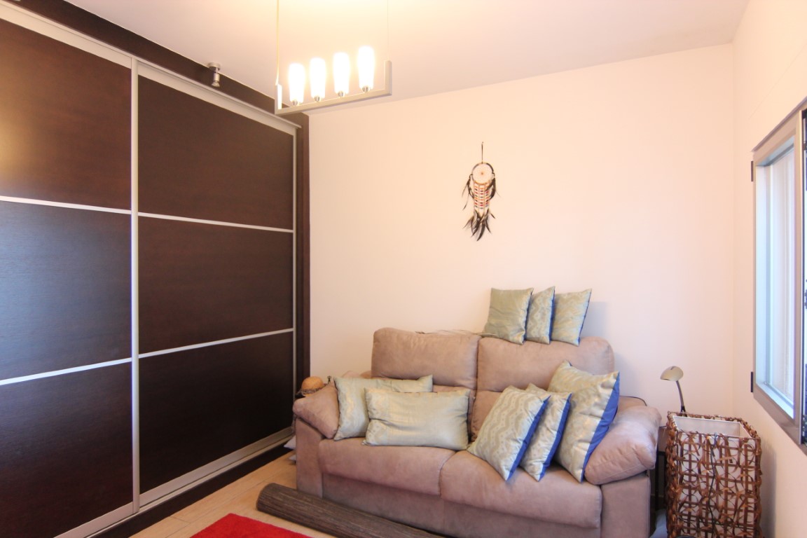 Schlafzimmer mit großem Einbauschrank aus dunklem Holz und Schiebetüren, einem Sofa mit Zierkissen und einer modernen vierflammigen Pendelleuchte.