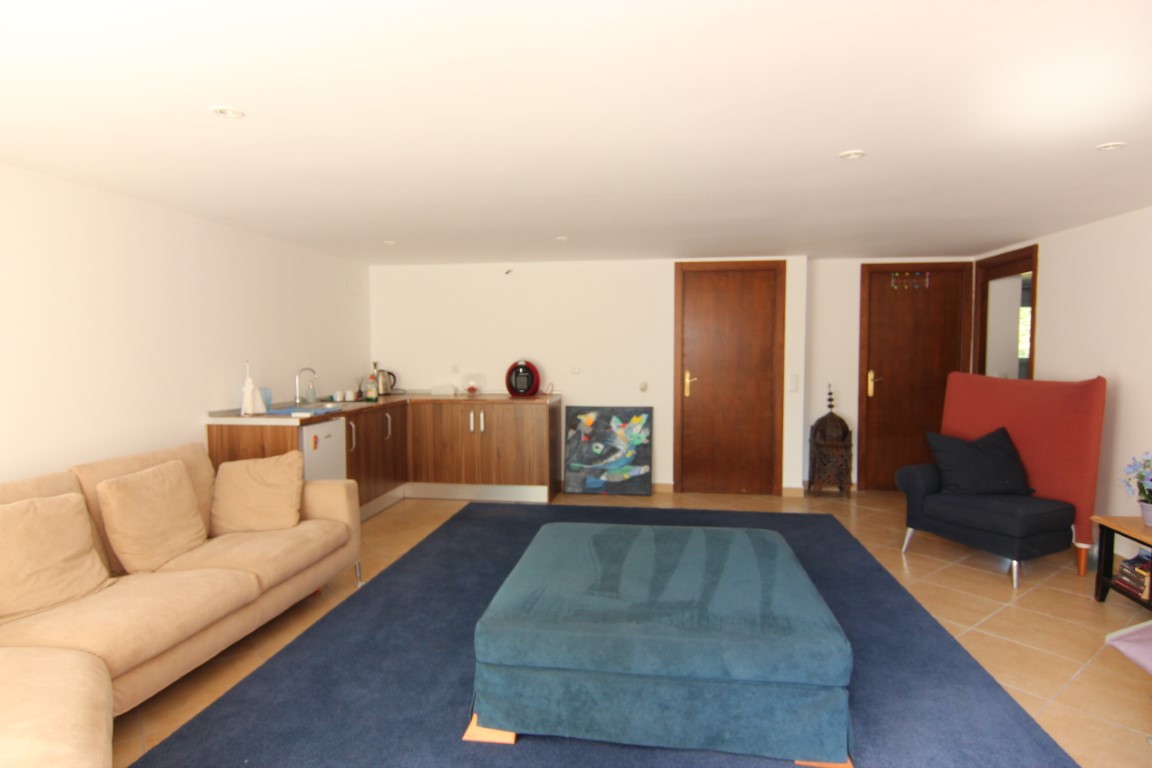 Wohnbereich des Gästeapartments mit integrierter Küchenzeile, Einbaustrahlern, Fliesenboden und direktem Zugang zu den Schlafzimmern durch Holztüren.