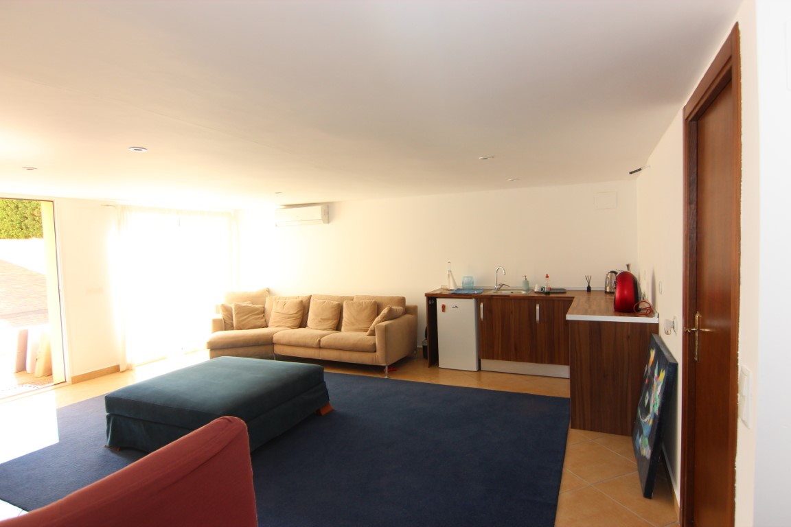 Wohnbereich des Gästeapartments mit integrierter Küchenzeile, großem Ecksofa, Klimaanlage und direktem Zugang zum Außenbereich.