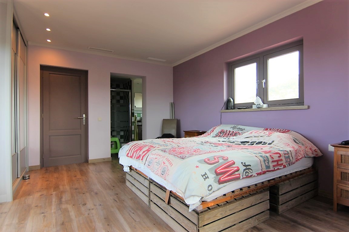 Doppelzimmer mit fliederfarbenen Wänden, Holzboden und einem Bettgestell aus Holzpaletten. Mit Einbauschränken, Deckenspots und Zugang zum En-Suite-Bad.