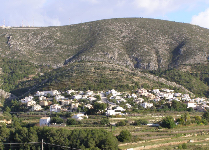 Panoramablick auf einen terrassierten Hang in Benitachell mit weißen Villen vor einer markanten Bergkulisse und typisch mediterraner Vegetation.