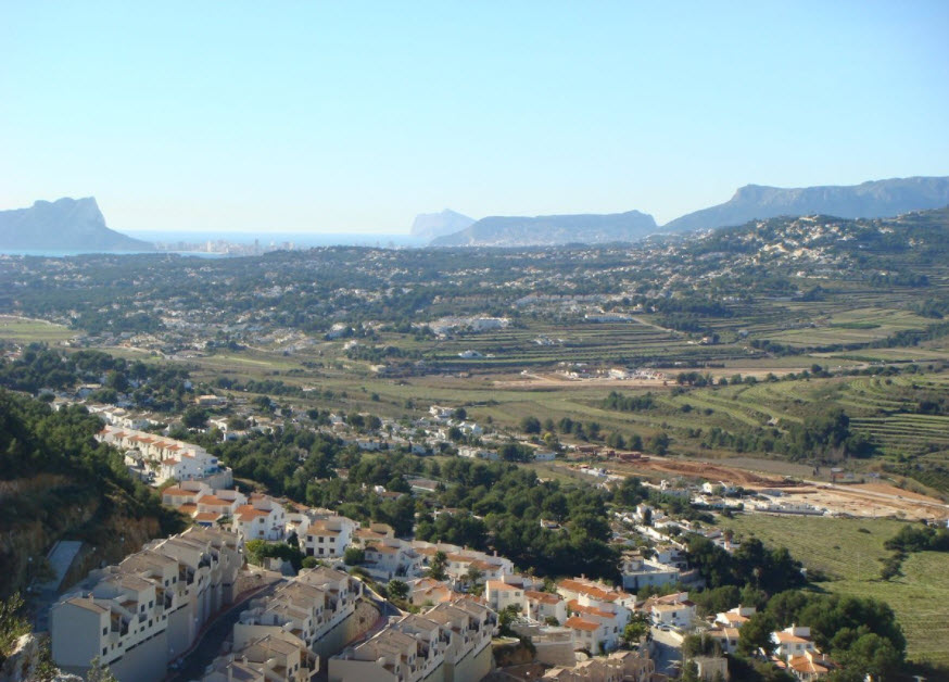 Panoramablick von Benitachell über das Tal bis zum Mittelmeer, mit terrassierten Landschaften und markanten Felsformationen der Costa Blanca in der Ferne.