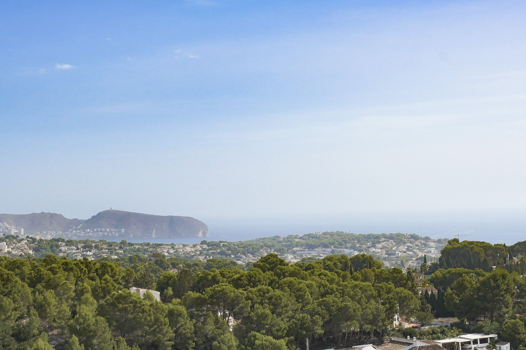Erhöhter Panoramablick vom Grundstück über einen mediterranen Pinienwald, Wohngebiete an der Küste und das Meer mit einer markanten Landzunge.
