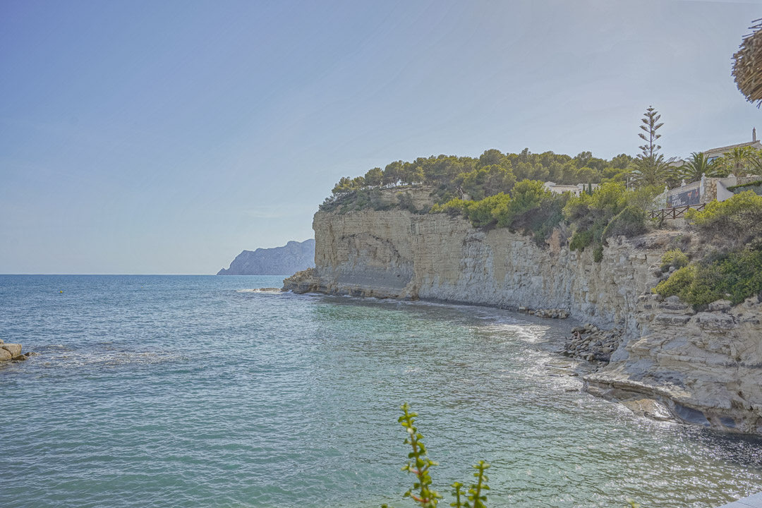 Panoramablick auf die Kalksteinfelsen und das türkisfarbene Mittelmeer nahe dem Strand La Fustera, gesäumt von Pinien und einer felsigen Küstenlinie.
