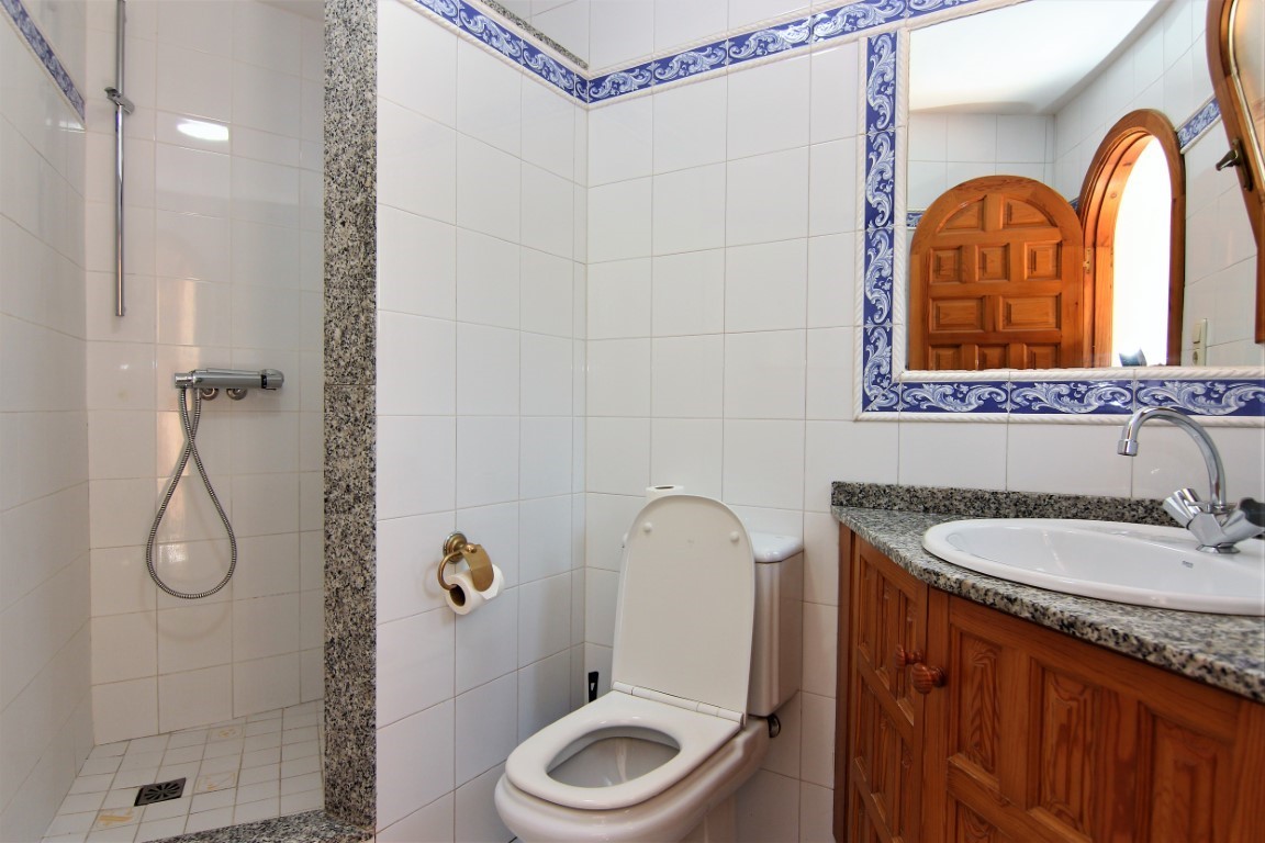 Badezimmer mit begehbarer Dusche, Granit-Arbeitsplatte, Holzunterschrank und weißen Fliesen mit blauen Zierborten.