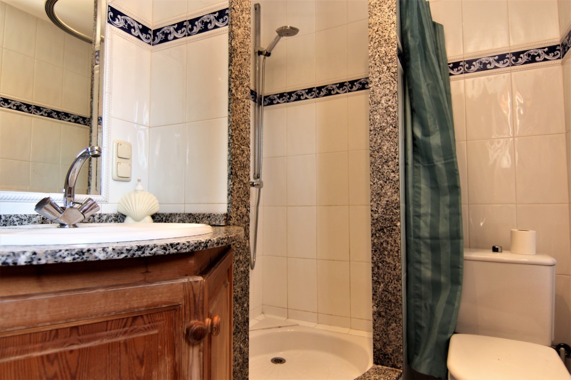 Badezimmer mit Granit-Arbeitsplatte, Holzunterschrank, integrierter Dusche mit Steinrahmen und weißen Wandfliesen mit blauer Zierbordüre.
