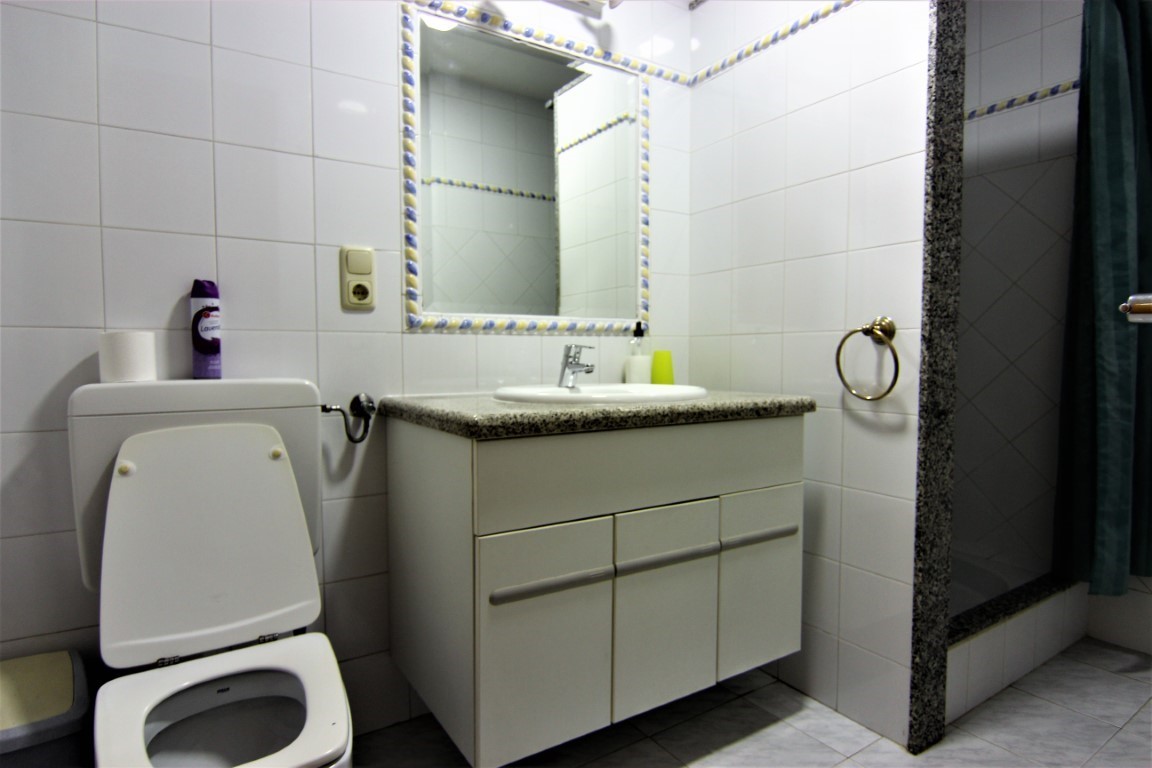 Badezimmer mit Waschtisch aus Granit, dekorativ eingefasstem Spiegel und einer Dusche mit Natursteinrahmen und dunklem Vorhang.