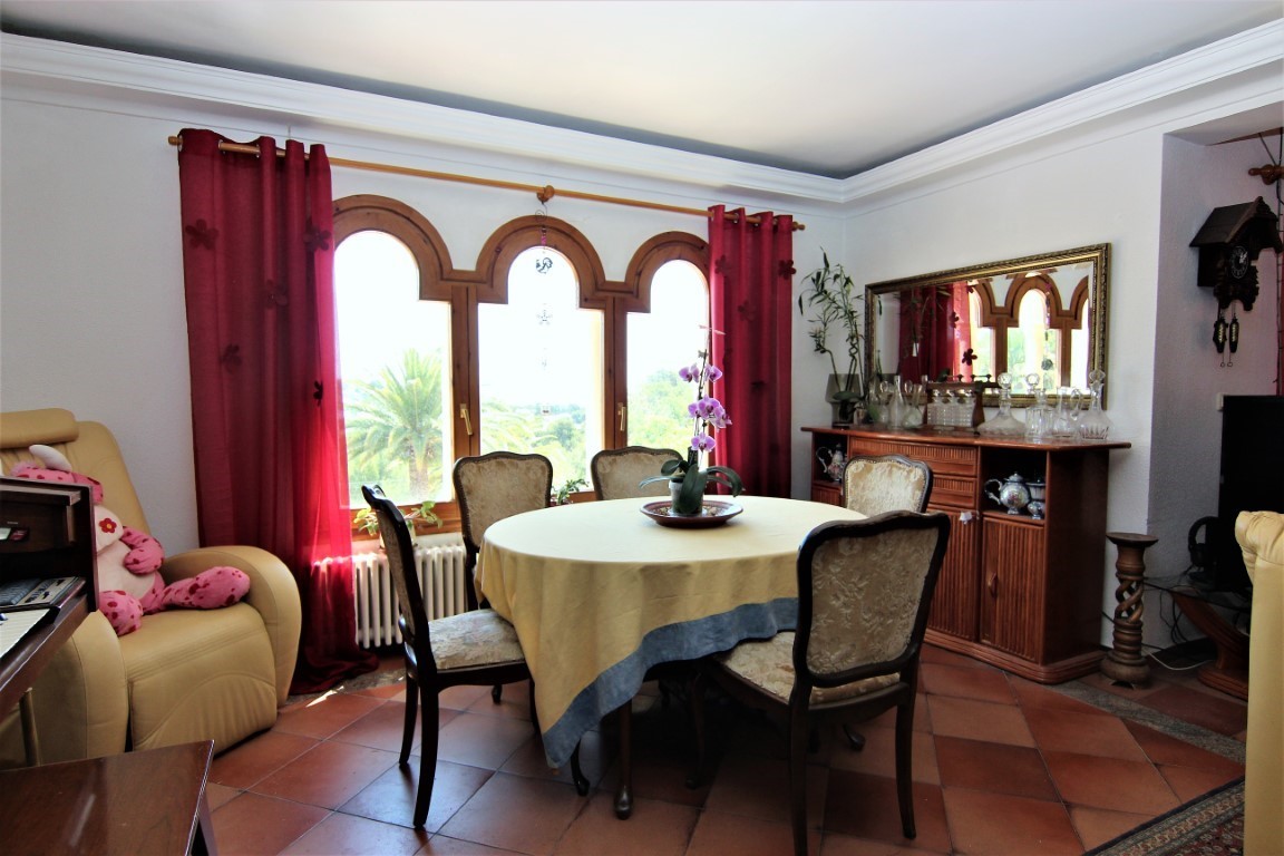 Essbereich mit rundem Tisch, gepolsterten Stühlen und dreifachem Rundbogenfenster. Terrakotta-Fliesenboden und ein klassisches Holz-Sideboard mit Spiegel.