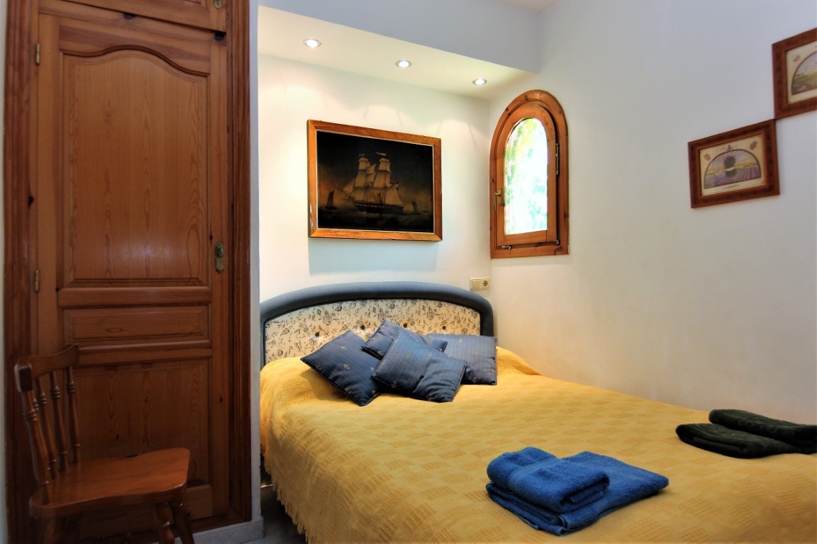 Gemütliches Schlafzimmer mit Einbauschrank aus Holz, traditionellem Rundbogenfenster und Deckenspots über dem verzierten Kopfteil.