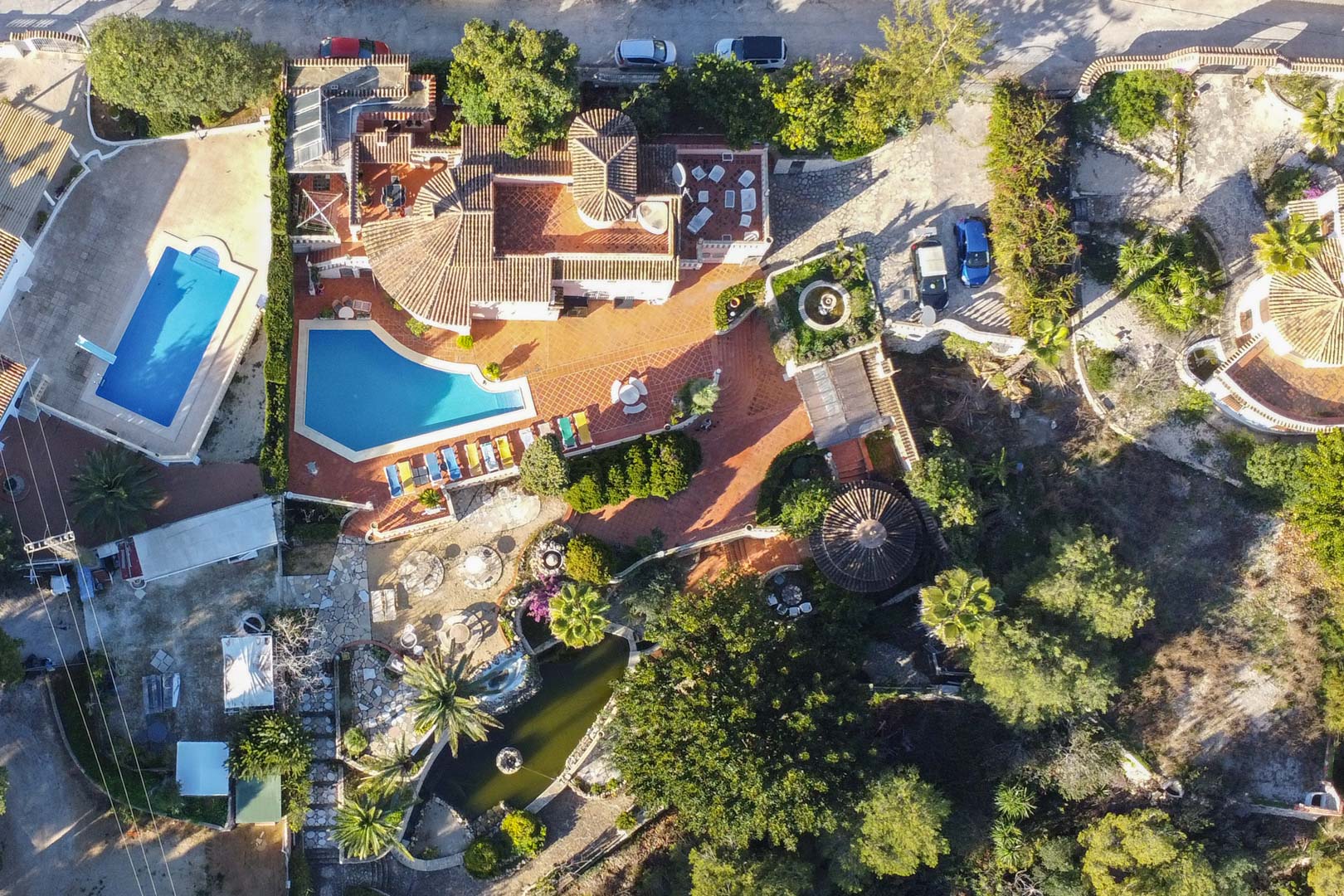 Luftaufnahme des Anwesens mit dem geschwungenen Pool, weitläufigen Terracotta-Terrassen, einem großen Gartenteich und der mediterranen Bepflanzung des gesamten Grundstücks.
