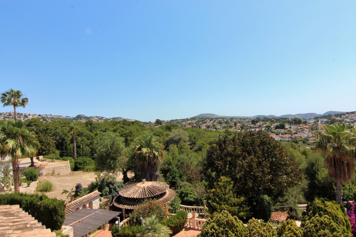 Panoramablick von der oberen Terrasse auf den mediterranen Garten mit Palmen, einem runden Ziegelpavillon und den umliegenden Wohnhügeln in der Ferne.