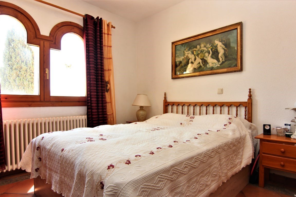 Schlafzimmer mit Doppelbett, hölzernem Kopfteil und traditionellen Rundbogenfenstern. Ausgestattet mit Terrakottaboden und klassischem Heizkörper.