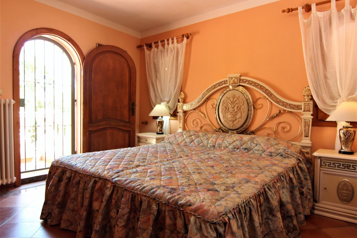 Schlafzimmer mit ornamentalem klassischem Kopfteil, pfirsichfarbenen Wänden und einer gewölbten Holztür zum Außenbereich.