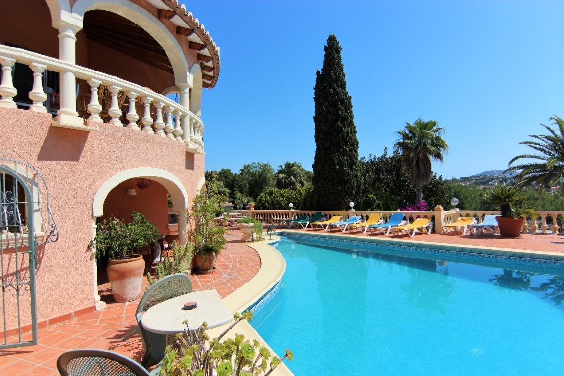 Terracotta-Terrasse mit geschwungenem Pool, farbigen Liegen und mediterraner Fassade mit klassischen Rundbögen und weißen Balustraden.