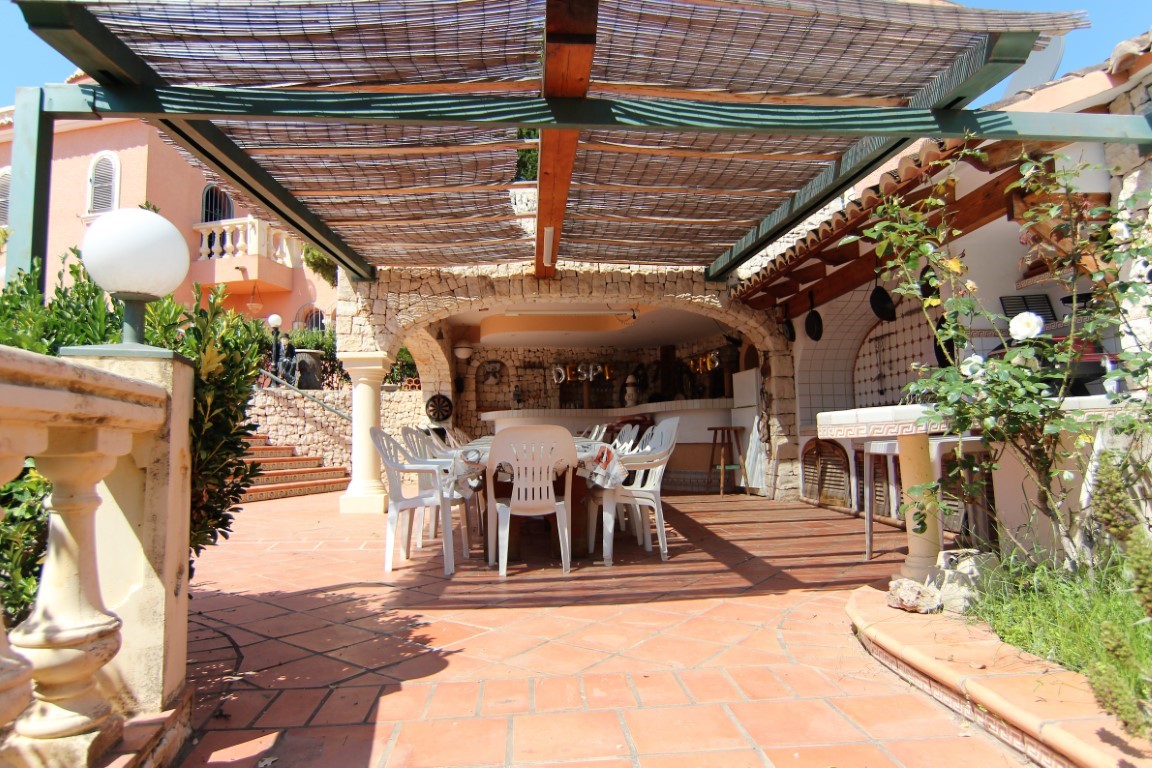 Überdachte Außenterrasse mit Schilfrohr-Pergola, großem Essbereich und Außenküche unter rustikalen Steinbögen mit klassischem Terrakottaboden.