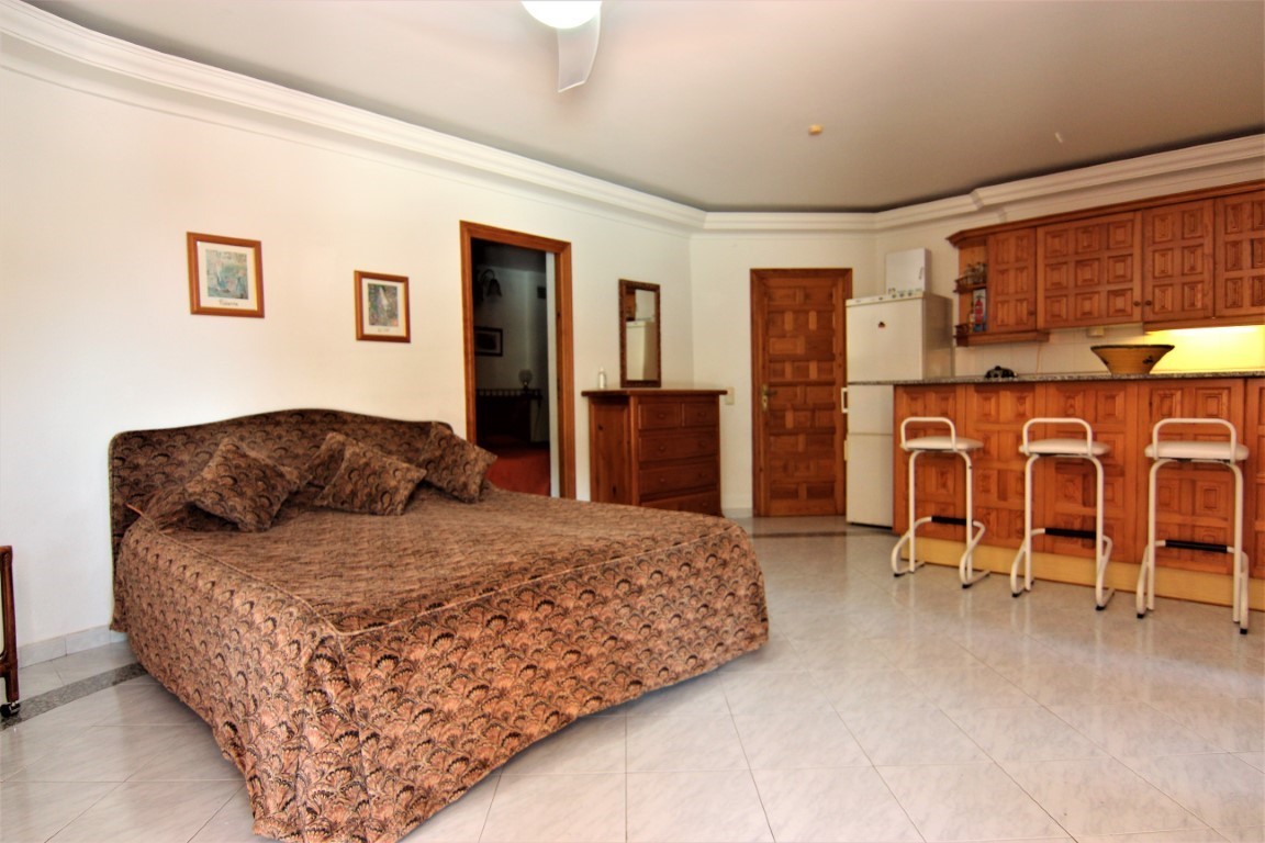 Unabhängiges Studio-Apartment mit Doppelbett, integrierter Holzküche mit Frühstücksbar, Hockern und hellem Fliesenboden.